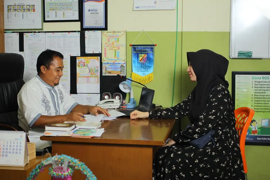 Mahasiswa belajar menggunakan buku dan laptop di ruang sederhana